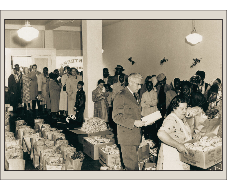 Vintage black and white photo of a group of people in line being given boxes of food for the holiday